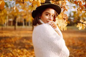 Woman in a white sweater under a tree with yellow leaves during the autumn season