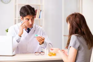 A man doctor is showing a woman a bottle of eye drops