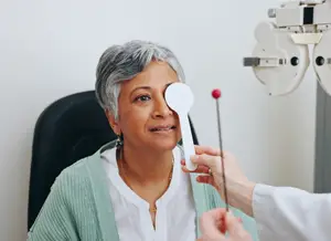 An elderly woman is having her eyes examined by a doctor in an office.