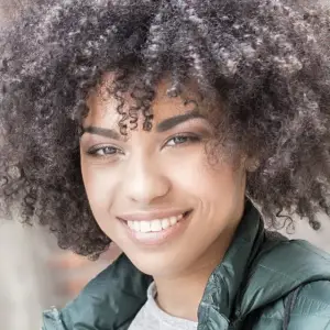 A smiling woman with curly hair and a green jacket