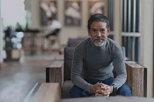 A man with a beard is sitting on a couch in a room with a glass wall and a wooden floor