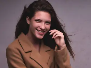 Portrait of a woman with long dark hair wearing a brown coat and smiling while posing for a photo