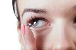 Close up of a woman with pink nails putting in a contact lens.