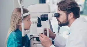A man doctor is examining a young girl's eyes using a device in an office.