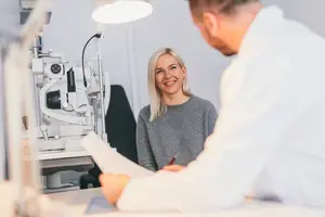A doctor is consulting with a patient in an eye clinic, while a machine is behind them.