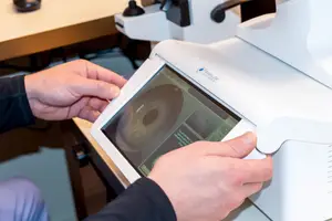 A person is holding an optical machine with a screen displaying an image of an eye