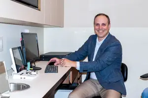 A man sitting at a desk with a monitor and keyboard in an office room.