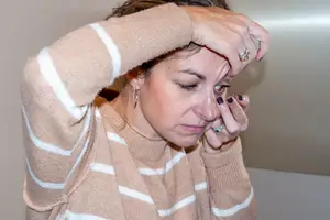 woman with brown hair wearing a white and brown striped sweater crying