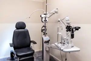 An optometrist's chair and examination equipment with a white table and beige wall in the background.