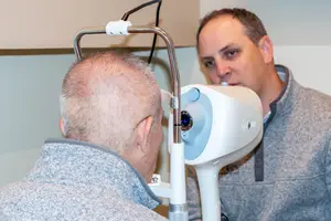An adult man is having his eyes checked with an eye exam machine in a clinic
