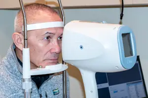 A man is looking into an optical machine with a white headband on his forehead.