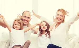 A family of four is sitting on a couch and posing for a photo with their arms raised