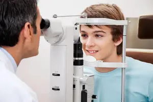A young boy is having his eyes examined by a doctor using a white machine.
