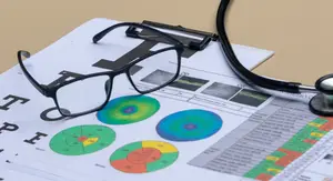 A stethoscope, eyeglasses, and an eye chart with a visual representation of different eye conditions are placed on a white sheet of paper on a beige surface