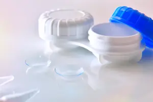 Two contact lens containers, one open showing lenses and one closed with a blue lid.
