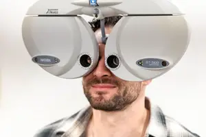 A man is having his eyes checked with a Nidek RT-5100 refractor in an optometrist's office.