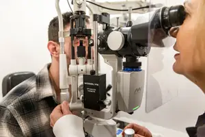 A man is getting his eyes checked by a woman doctor using a device