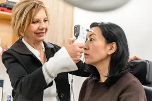 A woman is checking the eye of another woman with a device in a clinic.