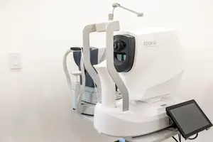 An eye examination machine with a tablet attached is placed on a white table in a room