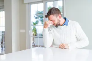 A man sitting at a table rubbing his eyes looking tired and exhausted