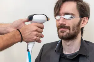 A man wearing a pair of smart glasses is being examined by another person using a device emitting light.