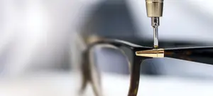 A pair of glasses with a golden-colored metal tip being adjusted by a machine