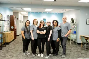 Seven people in matching uniforms stand in a room, one with his hands in his pockets, while another woman has her arms crossed.