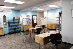 A room with desks and chairs for optometrists and shelves with eyeglass samples.