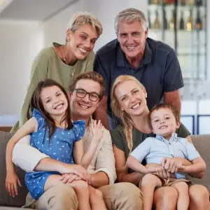 A family of five people, including two adults and three children, are sitting on a couch and smiling for a photograph.