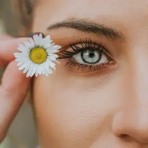 A woman's face with a daisy flower in her eye