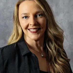 Close-up of a smiling woman with blonde hair wearing a black shirt and necklace