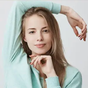 Woman with blonde hair in a mint blue shirt posing for a picture with her hands on her head and chin.