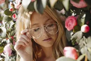 Blonde woman with sunglasses standing in front of pink flowers