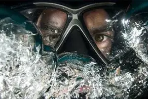 A person with a scuba mask and goggles submerged in water, with bubbles around them.