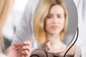A woman is placing a contact lens on her eye in front of a mirror