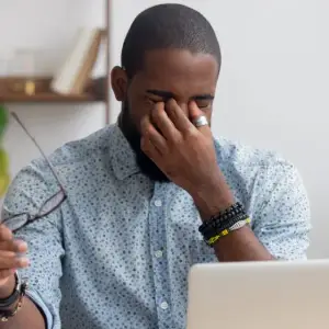 A man sitting in front of a laptop and covering his face with his hand