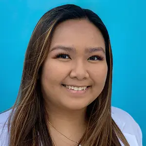 A smiling woman with brown hair and a white shirt standing in front of a blue background