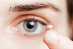 A close-up of a person's eye with a contact lens being inserted by their finger.