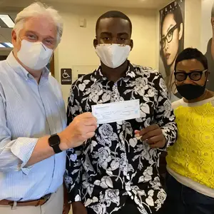 Three people in masks standing together in front of a wall with a poster of a woman wearing glasses and a sign for a handicapped bathroom