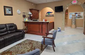 An interior of a waiting room with a leather couch, chairs, and a desk with a monitor.