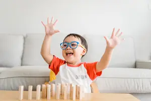 A young boy in glasses is playing with wooden blocks on a table in a living room