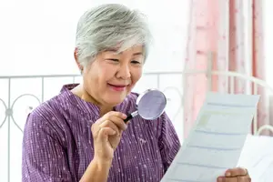 An older woman holding a magnifying glass and reading a document