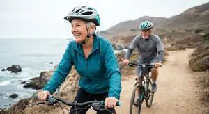 Two people in helmets biking near a coastline