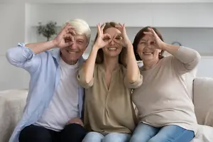 Three people sitting on a couch smiling and showing a peace sign with their fingers
