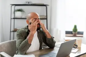 Man sitting at a desk rubbing his eyes with his hands