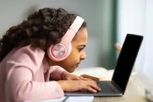 A girl wearing headphones is using a laptop on a desk.