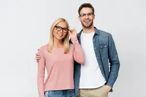 An adult man and woman stand close to each other and smile for a photo while wearing glasses.