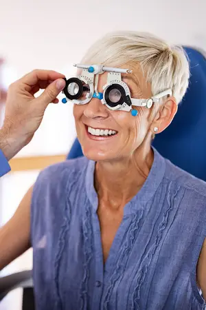 An older woman wearing an eye exam device is smiling at the camera