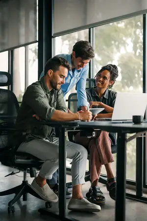 Three people working in a modern office, one man holding a bowl and smiling, another man smiling and looking at the woman, and a woman holding a laptop and smiling.