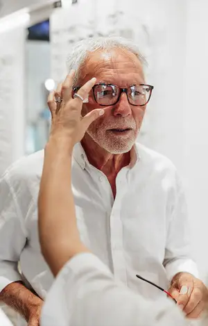An older man is adjusting his glasses with a woman's hand in front of him in a salon.